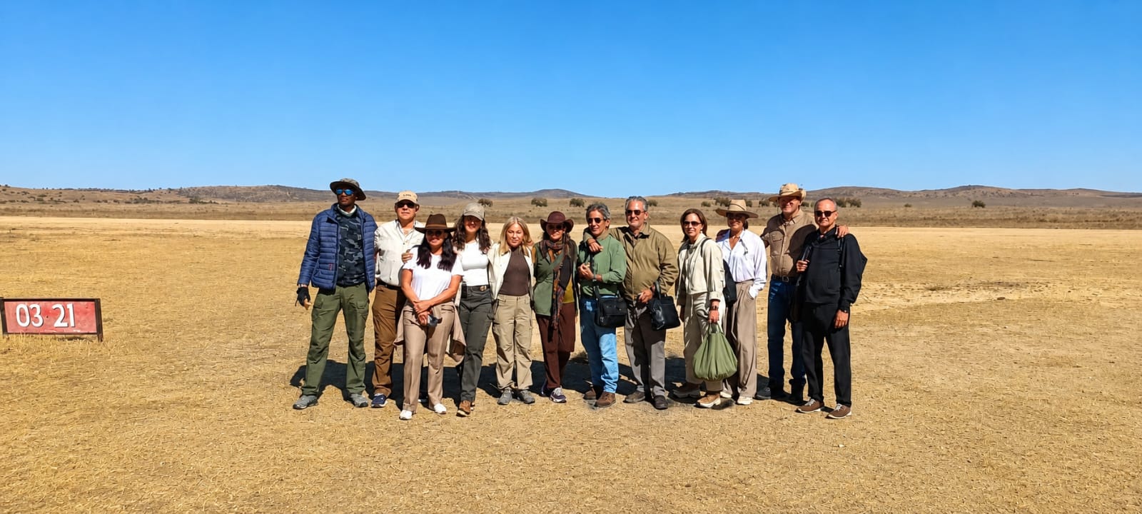 A group of guests standing together with their bags on a bush airstrip, a runway marker board beside them and open plains behind