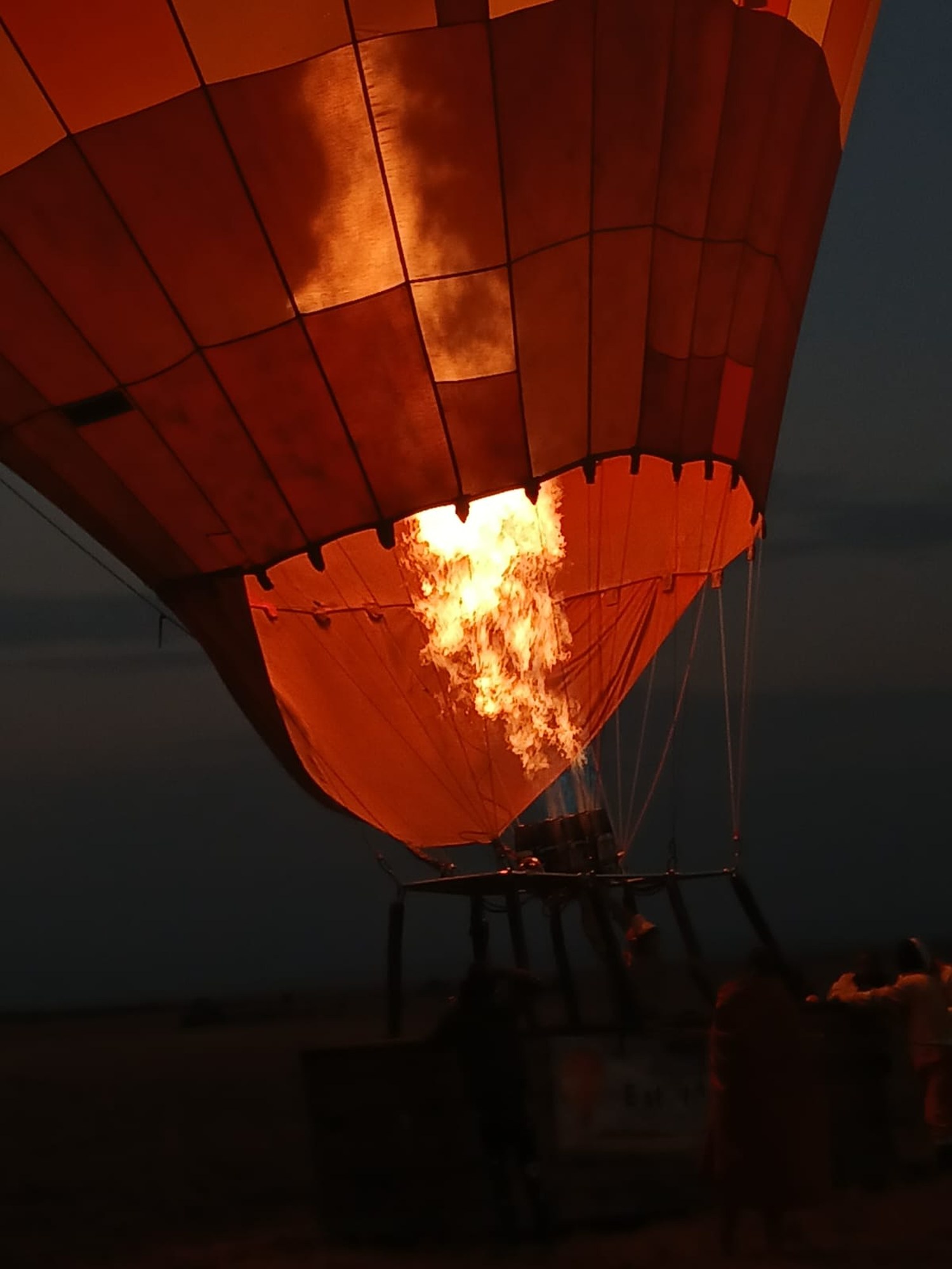 A balloon burner firing into the open mouth of an envelope before dawn, crew silhouetted below