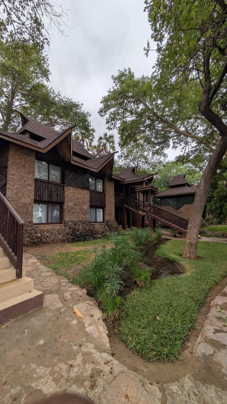 A two-storey timber and stone lodge building with an open staircase, set among trees