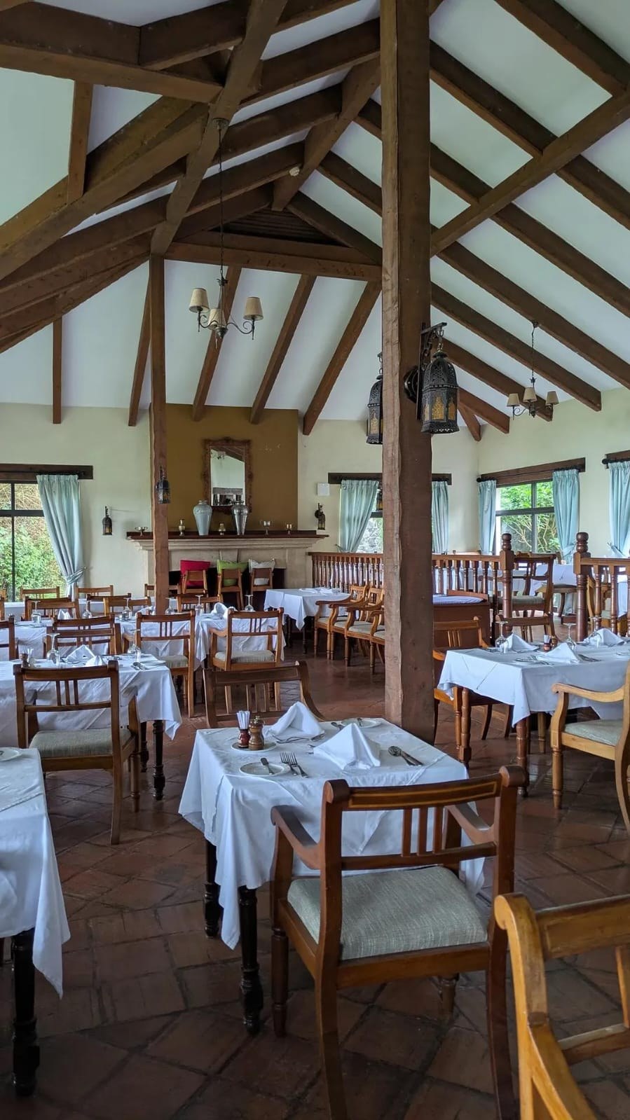 An empty lodge dining room set with white tablecloths under a high timber-beamed roof